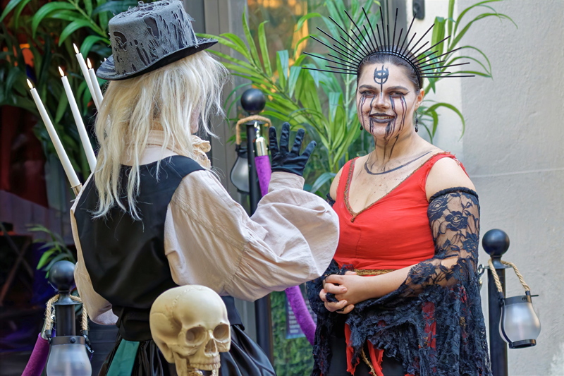 15 - Two women wearing detailed Halloween or gothic-themed costumes, including a top hat and a dramatic black-and-red ensemble with face